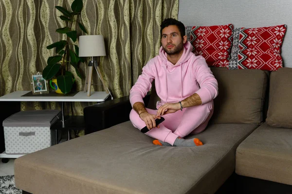 Joven adicto a la televisión hombre sentado en el sofá en casa y viendo la televisión usando control remoto, buscando aburrido y cansado, bombeando la película de comedia de otra persona o música en vivo por la noche — Foto de Stock