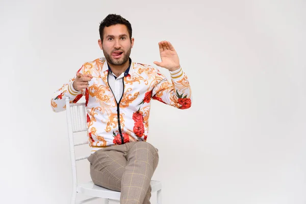 Concepto de moda para hombre. Retrato de un guapo modelo masculino, mostrando las manos, con una chaqueta blanca con un patrón floral, posando sobre un fondo blanco, menta en una silla. Pelo negro. Cerrar Studio Shot — Foto de Stock