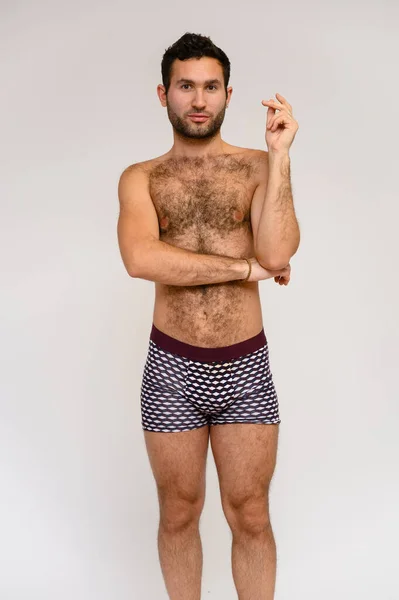 Retrato de un guapo modelo masculino con un cuerpo perfecto, de pie desnudo en pantalones cortos, posando sobre un fondo blanco. Pelo negro. Cerrar Studio Shot —  Fotos de Stock