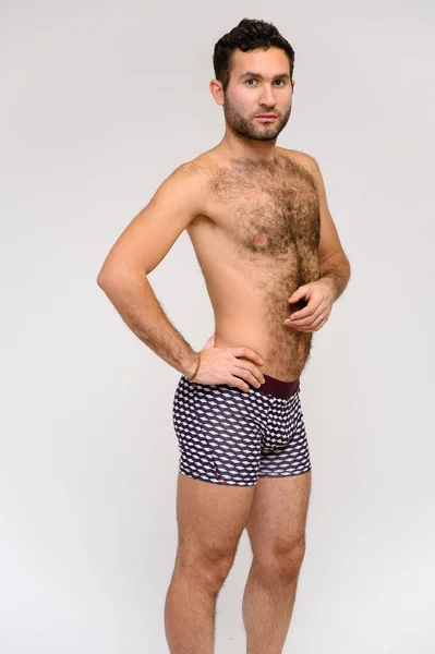 Portrait of a handsome male model with perfect body, standing naked in shorts, posing on a white background. Black hair. Close Studio Shot — Stock Photo, Image