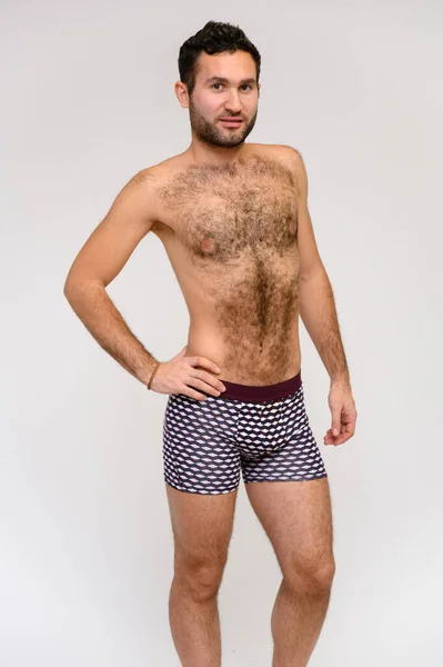 Retrato de un guapo modelo masculino con un cuerpo perfecto, de pie desnudo en pantalones cortos, posando sobre un fondo blanco. Pelo negro. Cerrar Studio Shot —  Fotos de Stock