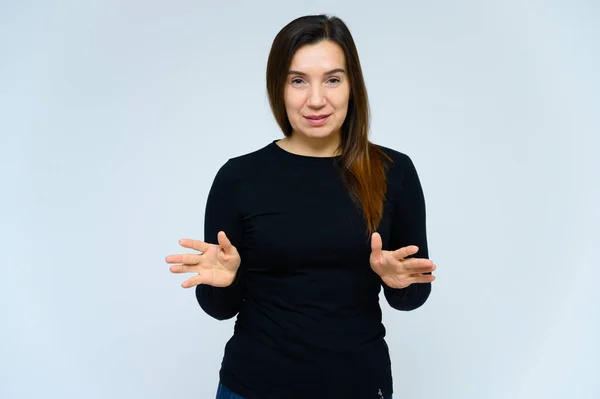 Retrato de una mujer adulta sin maquillaje con la piel limpia, con el pelo largo y castaño sobre su cara sobre un fondo blanco. Se para frente a la cámara con una camiseta negra, muestra sus manos emociones . — Foto de Stock