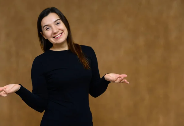 Retrato de uma mulher adulta sem maquiagem com pele limpa, com longos cabelos castanhos sobre o rosto em um fundo bege. Ele fica na frente da câmera em uma camiseta preta, mostra suas mãos emoções . — Fotografia de Stock