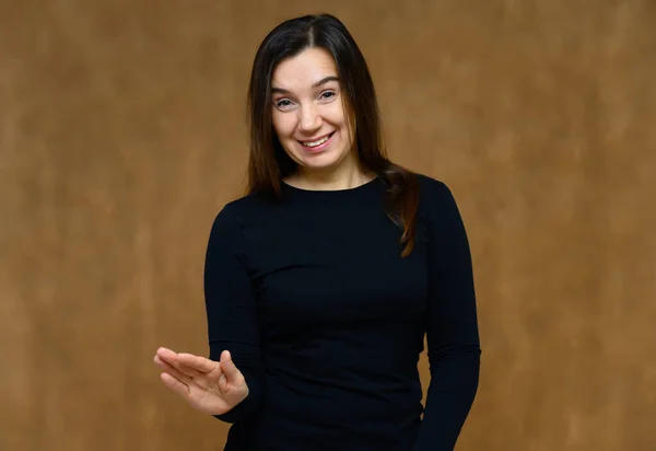 Retrato de una mujer adulta sin maquillaje con la piel limpia, con el pelo largo y castaño sobre su cara sobre un fondo beige. Se para frente a la cámara con una camiseta negra, muestra sus manos emociones . — Foto de Stock