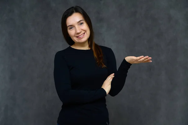 Retrato de una mujer adulta sin maquillaje con la piel limpia, con el pelo largo y castaño sobre su cara sobre un fondo gris. Se para frente a la cámara con una camiseta negra, muestra sus manos emociones . — Foto de Stock