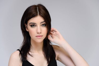 Uzun siyah saçlı, gri arka planda temiz tenli güzel bir kızın yakın plan portresi. Yüze makyaj malzemesi, harika makyaj, modaya uygun saç stili..