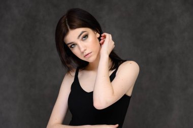 Gri arka planda, uzun siyah saçlı güzel bir kızın yakın plan portresi. Kameranın önünde duruyor, ellerini farklı pozlarda ve farklı duygularla gösteriyor..