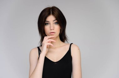 Beyaz arka planda uzun siyah saçlı güzel bir kızın yakın plan portresi. Kameranın önünde duruyor, ellerini farklı pozlarda ve farklı duygularla gösteriyor..