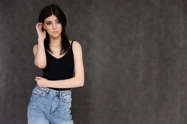 Retrato de una joven estudiante bonita con el pelo largo y negro, sobre un fondo gris. Se para justo delante de la cámara, mostrando sus manos en diferentes poses con diferentes emociones . — Foto de Stock