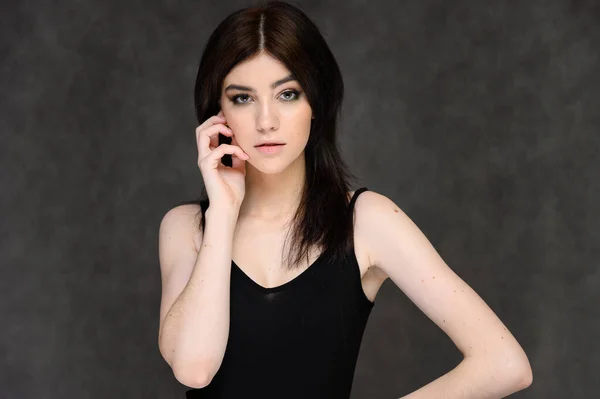 Retrato de cerca de una joven estudiante bonita con el pelo largo y negro, sobre un fondo gris. Se para justo delante de la cámara, mostrando sus manos en diferentes poses con diferentes emociones . — Foto de Stock