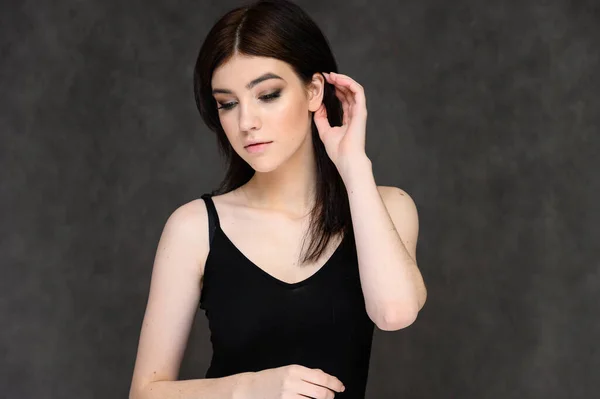 Retrato de cerca de una joven estudiante bonita con el pelo largo y negro, sobre un fondo gris. Se para justo delante de la cámara, mostrando sus manos en diferentes poses con diferentes emociones . — Foto de Stock