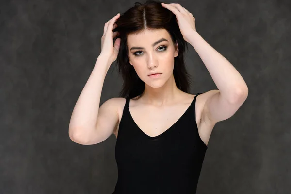 Retrato de cerca de una joven estudiante bonita con el pelo largo y negro, sobre un fondo gris. Se para justo delante de la cámara, mostrando sus manos en diferentes poses con diferentes emociones . — Foto de Stock