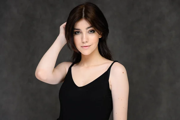 Retrato de cerca de una joven estudiante bonita con el pelo largo y negro, sobre un fondo gris. Se para justo delante de la cámara, mostrando sus manos en diferentes poses con diferentes emociones . — Foto de Stock