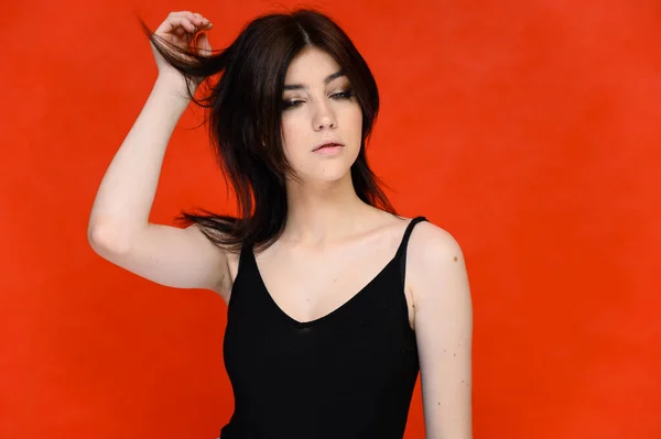 Retrato de cerca de una joven estudiante bonita con el pelo largo y negro, sobre un fondo rojo. Se para justo delante de la cámara, mostrando sus manos en diferentes poses con diferentes emociones . — Foto de Stock