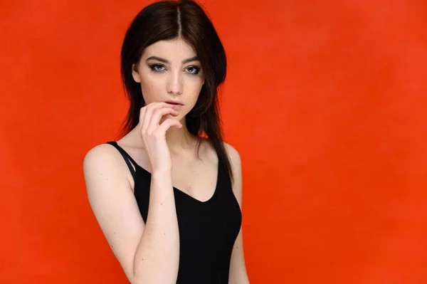 Retrato de cerca de una joven estudiante bonita con el pelo largo y negro, sobre un fondo rojo. Se para justo delante de la cámara, mostrando sus manos en diferentes poses con diferentes emociones . — Foto de Stock