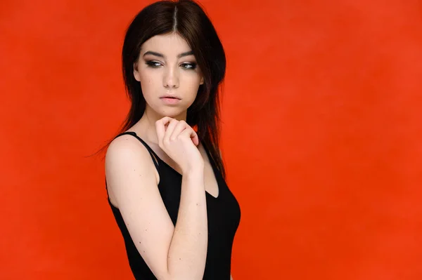 Retrato de cerca de una joven estudiante bonita con el pelo largo y negro, sobre un fondo rojo. Se para justo delante de la cámara, mostrando sus manos en diferentes poses con diferentes emociones . — Foto de Stock