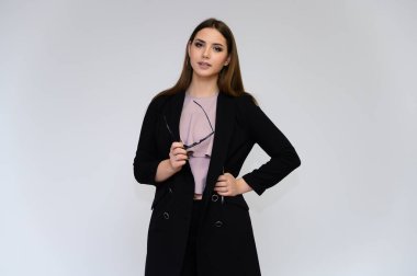 Beyaz bir arka planda, siyah takım elbiseli, uzun siyah saçlı, güzel bir sekreterin yakın plan portresi. Farklı pozlarda kameranın önünde durarak..