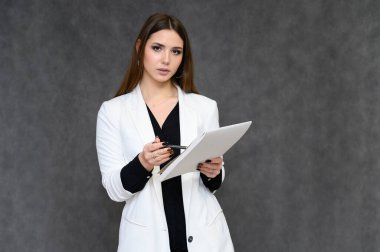 Gri bir arka planda, iş elbisesi içinde uzun siyah saçlı, güzel bir sekreterin yakın plan portresi. Farklı pozlarda kameranın önünde durarak..
