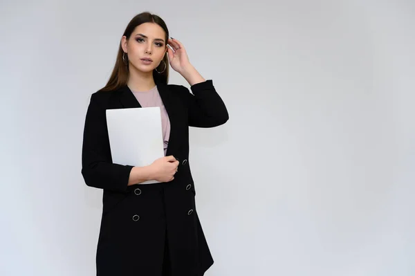 Retrato de cerca de una joven secretaria guapa con el pelo largo y negro en un traje de negocios negro, sobre un fondo blanco. De pie justo delante de la cámara en diferentes poses con emociones . — Foto de Stock