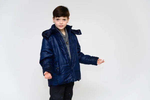 Le concept de vêtements d'hiver et chauds pour un adolescent. Portrait d'un petit garçon sur fond blanc vêtu d'une veste et d'un pantalon d'hiver. Se tient devant la caméra dans différentes poses avec des émotions . — Photo
