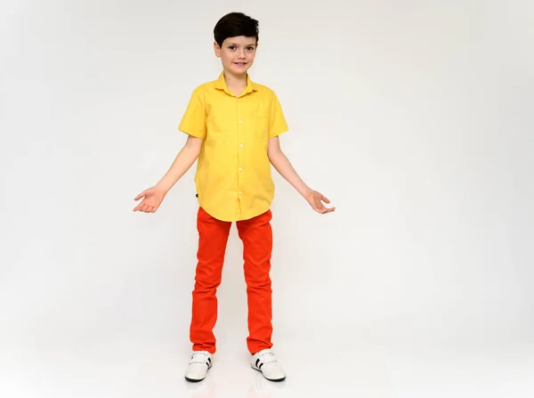 Adolescent écolier garçon concept montre émotion. Photo pleine longueur d'un enfant en pantalon rouge et une chemise jaune sur fond blanc en studio. Se tient devant la caméra dans différentes poses . — Photo