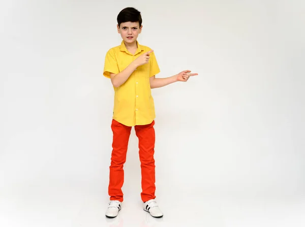 Teenager Schoolboy Boy Concept Shows Emotion. Full-length photo of a child in red pants and a yellow shirt on a white background in studio. Stands in front of the camera in various poses. — Stock Photo, Image