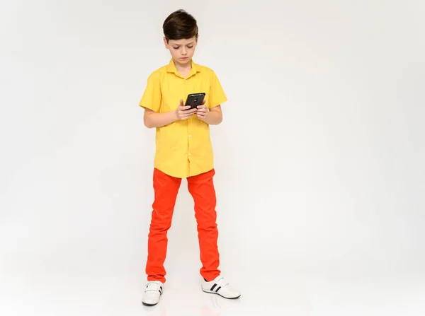 Begreppet tonårspojke som pratar i telefon. Fullängdare foto av ett barn i röda byxor och en gul skjorta på en vit bakgrund i studio. Står framför kameran i olika poser. — Stockfoto
