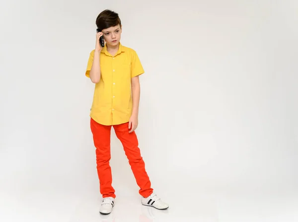 Концепция подростка, разговаривающего по телефону. Полная фотография ребенка в красных штанах и желтая рубашка на белом фоне в студии. Стоят перед камерой в различных позах . — стоковое фото