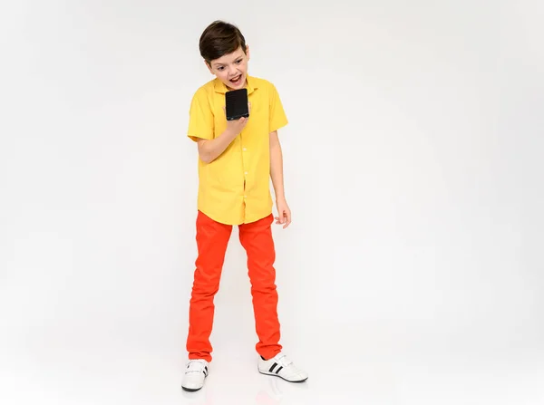 Concept de garçon d'école adolescent parlant au téléphone. Photo pleine longueur d'un enfant en pantalon rouge et une chemise jaune sur fond blanc en studio. Se tient devant la caméra dans différentes poses . — Photo