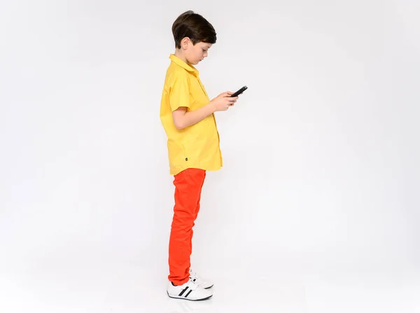 Концепция подростка, разговаривающего по телефону. Полная фотография ребенка в красных штанах и желтая рубашка на белом фоне в студии. Стоят перед камерой в различных позах . — стоковое фото