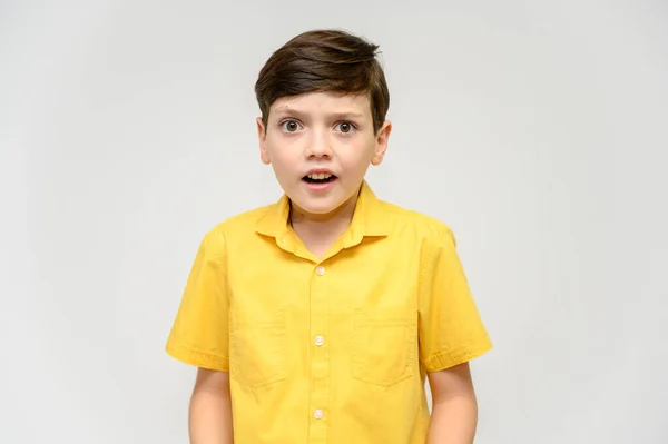 Koncepció fiú tizenéves mutatja utánozza a viselkedését hősök különböző filmekben. Egy fehér hátterű, sárga inges gyermek portréja. A kamera előtt állni, érzelmekkel pózolva.. — Stock Fotó