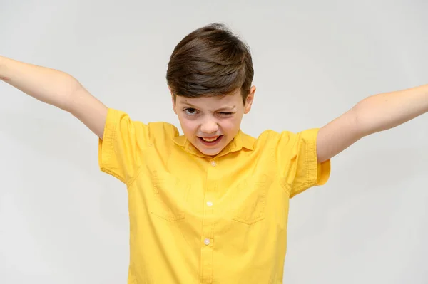 Concept boy teenager shows imita o comportamento de heróis de diferentes filmes. Retrato de uma criança em um fundo branco em uma camisa amarela. De pé na frente da câmera em poses com emoções . — Fotografia de Stock
