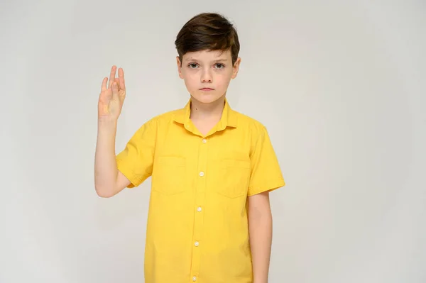 Concept boy teenager shows imitates the behavior of heroes from different movies. Portrait of a child on a white background in a yellow shirt. Standing in front of the camera in poses with emotions. — Stock Photo, Image