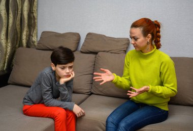 Ergen bir çocuk ve farklı duygularla kanepede oturan aile içi anlaşmazlık konseptinde mutsuz bir anne. Çocuk ve anne birbirlerinden mutsuzlar. Farklı pozlarda oturun..