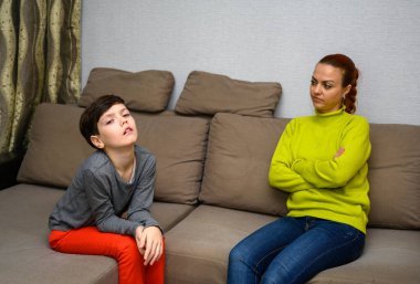 Ergen bir çocuk ve farklı duygularla kanepede oturan aile içi anlaşmazlık konseptinde mutsuz bir anne. Çocuk ve anne birbirlerinden mutsuzlar. Farklı pozlarda oturun..