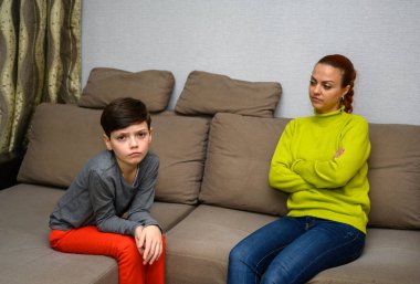 Ergen bir çocuk ve farklı duygularla kanepede oturan aile içi anlaşmazlık konseptinde mutsuz bir anne. Çocuk ve anne birbirlerinden mutsuzlar. Farklı pozlarda oturun..