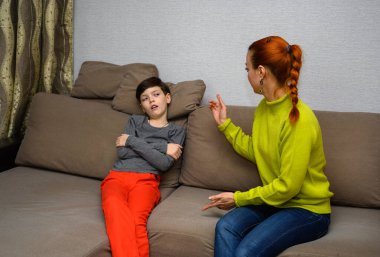 Ergen bir çocuk ve farklı duygularla kanepede oturan aile içi anlaşmazlık konseptinde mutsuz bir anne. Çocuk ve anne birbirlerinden mutsuzlar. Farklı pozlarda oturun..