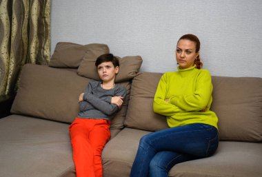 Ergen bir çocuk ve farklı duygularla kanepede oturan aile içi anlaşmazlık konseptinde mutsuz bir anne. Çocuk ve anne birbirlerinden mutsuzlar. Farklı pozlarda oturun..