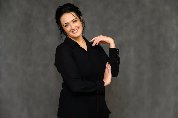 Concepto de mujer de negocios. Retrato de una guapa morena sobre fondo gris en blusa negra. Se para frente a la cámara, sonríe, habla en varias poses con emociones . — Foto de Stock