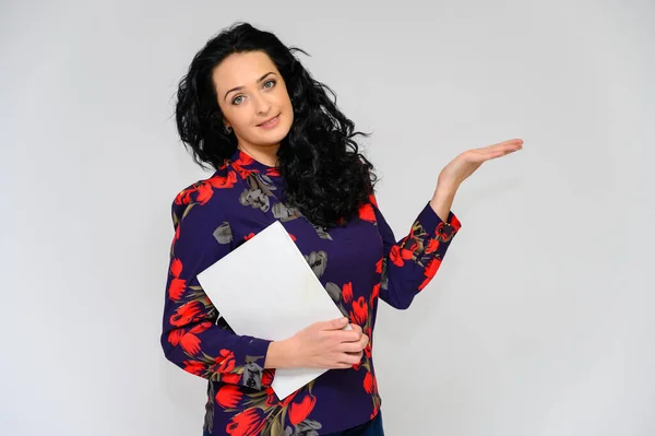 Retrato de una guapa morena con el pelo largo y rizado sobre un fondo blanco en una blusa de color con una carpeta en las manos. Se para frente a la cámara, sonríe, habla en varias poses . — Foto de Stock