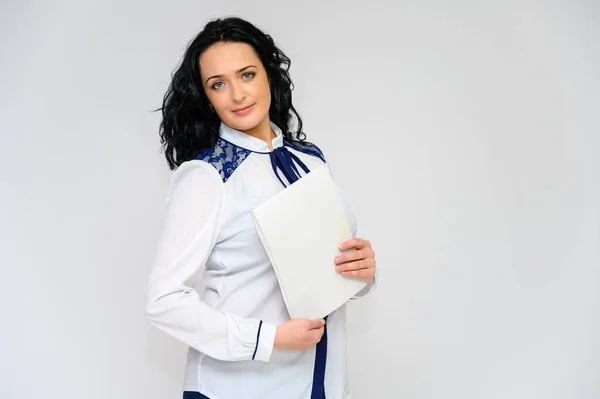 Retrato de una guapa morena con el pelo largo y rizado sobre un fondo blanco en blusa blanca con una carpeta en las manos. Se para frente a la cámara, sonríe, habla en varias poses . — Foto de Stock