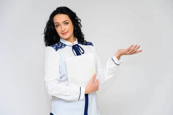 Retrato de una guapa morena con el pelo largo y rizado sobre un fondo blanco en blusa blanca con una carpeta en las manos. Se para frente a la cámara, sonríe, habla en varias poses . — Foto de Stock