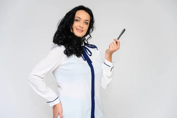 Retrato de una guapa morena con el pelo largo y rizado sobre un fondo blanco en blusa blanca. Se para frente a la cámara, sonríe, habla en varias poses . — Foto de Stock