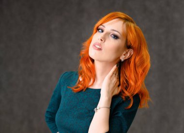 Kızıl saçlı güzel bir kızın yakın plan portresi mükemmel makyajlı ve gri arka planda parlak kıvırcık saçlı. Güzellik konsepti, güzel saç stili ve makyaj malzemesi..