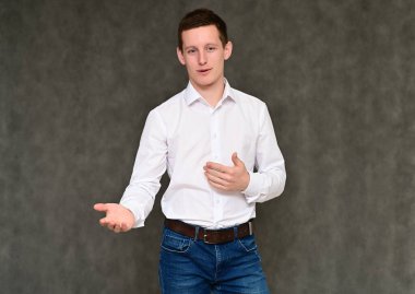 Hoş bir genç adamın kameraya konuşması fikri. Mavi kotlu gri arka planda bir sekreter portresi ve çeşitli pozlarda beyaz gömlek..