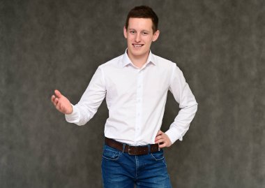 Hoş bir genç adamın kameraya konuşması fikri. Mavi kotlu gri arka planda bir sekreter portresi ve çeşitli pozlarda beyaz gömlek..