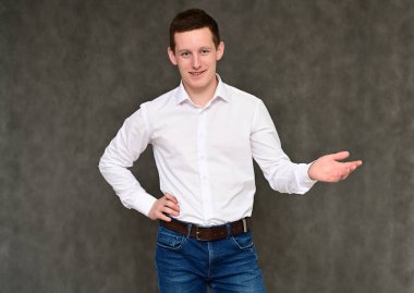 Hoş bir genç adamın kameraya konuşması fikri. Mavi kotlu gri arka planda bir sekreter portresi ve çeşitli pozlarda beyaz gömlek..