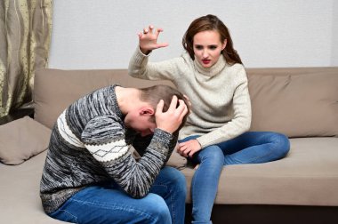 Aile çatışması kavramı. Genç mutsuz bir ailenin portresi: kızgın esmer kız ve evdeki kanepede oturan hoşnutsuz adam. Tatminsiz bir eş kocasını azarlar..