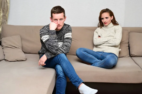家庭冲突的概念。 一个不快乐的年轻家庭的画像：愤怒的黑发女孩和不高兴的家伙穿着毛衣躺在房间里的沙发上。 不满意的妻子责备丈夫. — 图库照片
