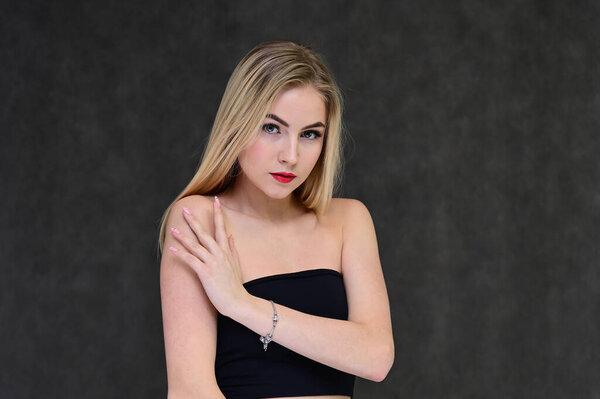 The concept of fashionable glamor, cosmetics and beauty with a pretty girl. Portrait of a fashionable beautiful blonde model with long hair, great makeup, on a gray background.